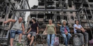 Menschen vor zerstörtem Gebäude in Mariupol.