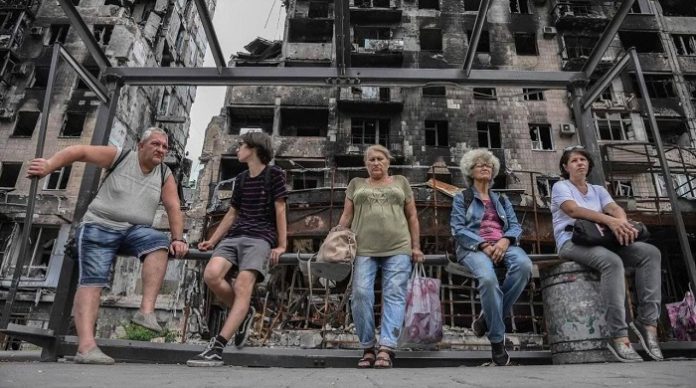 Menschen vor zerstörtem Gebäude in Mariupol.