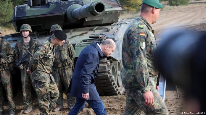 Bundeskanzler Olaf Scholz duckt sich vergangenen Oktober beim Vorübergehen an einem Kampfpanzer Leopard 2.